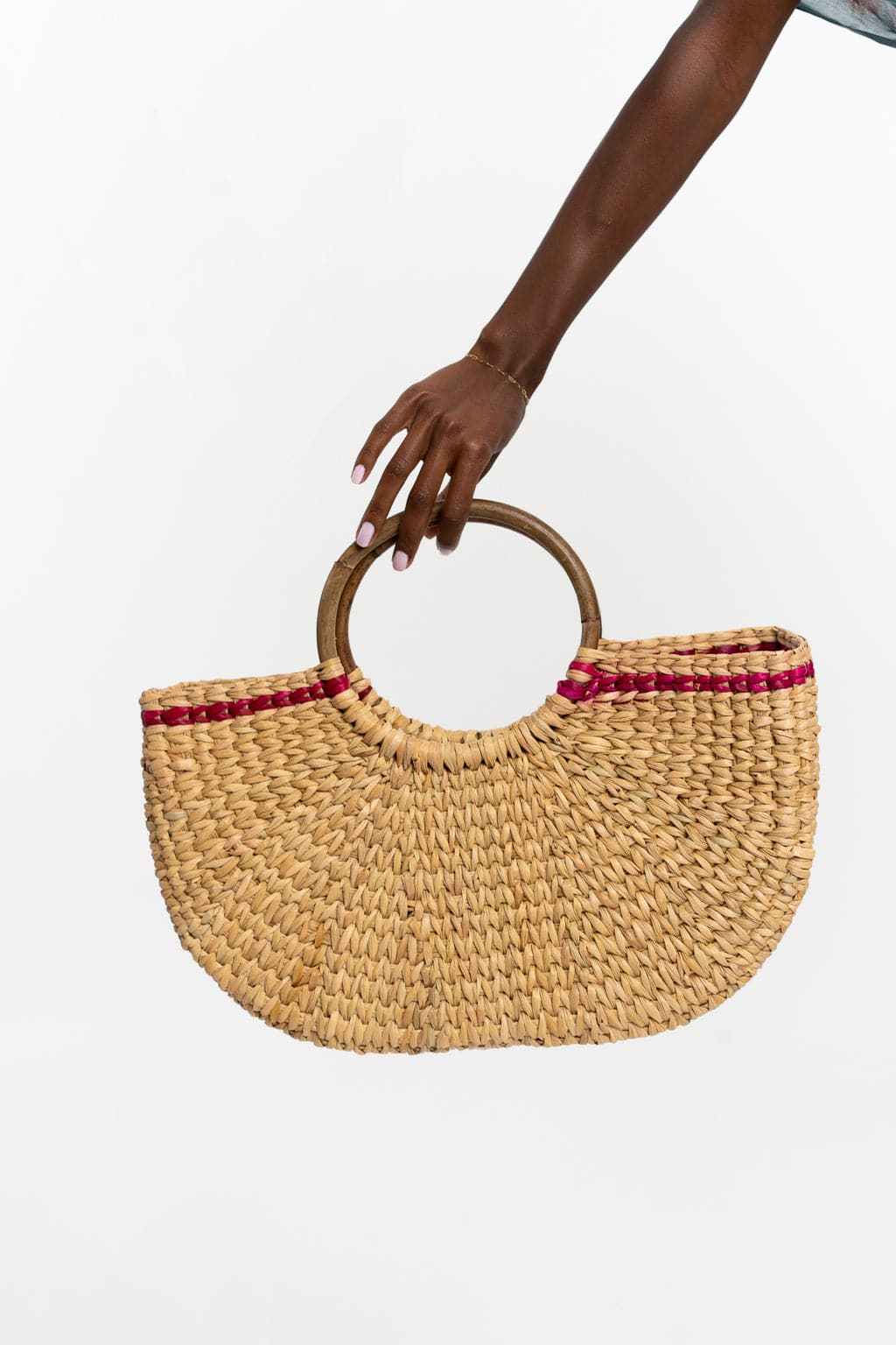 Black model holds out cane tote bag with circular bamboo wooden handle and pink stripe design.