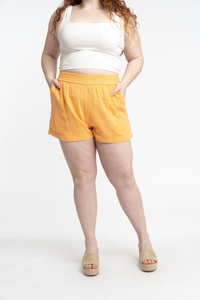 Young plus size model with long red hair is wearing yellow, double gauze, lounge camp shorts with hands in her pockets.