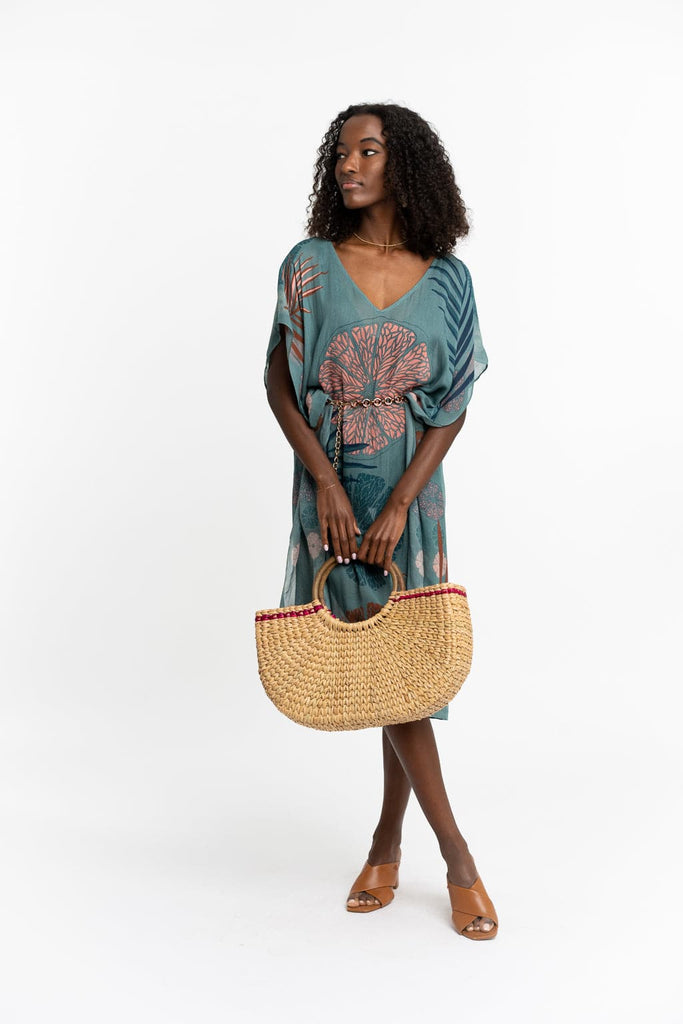 Young black model wearing a lightweight coverup and a gold chain belt holds a braided raffia straw tote bag with circular wooden handle