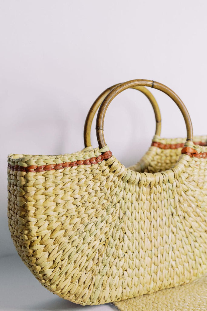 Hand-crafted natural grass tote bag with circular wooden handle and brown accent design braided into it.