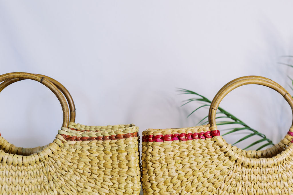 Two cane braided tote bags with a palm frond in the background.