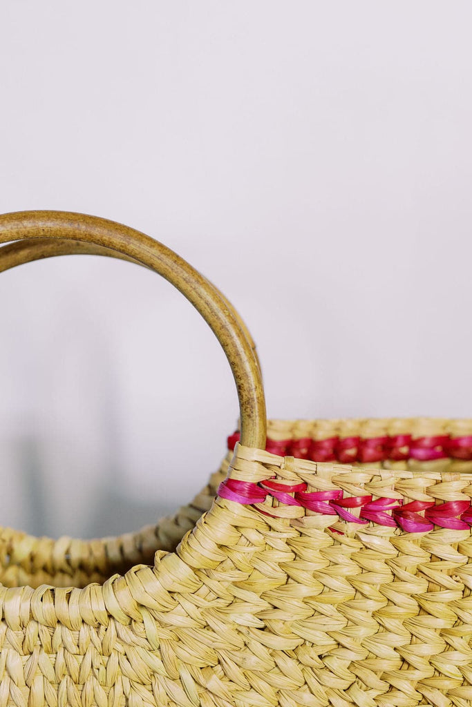 Close-up image of a braided tote bag with large wooden circular handle and pink straw design.